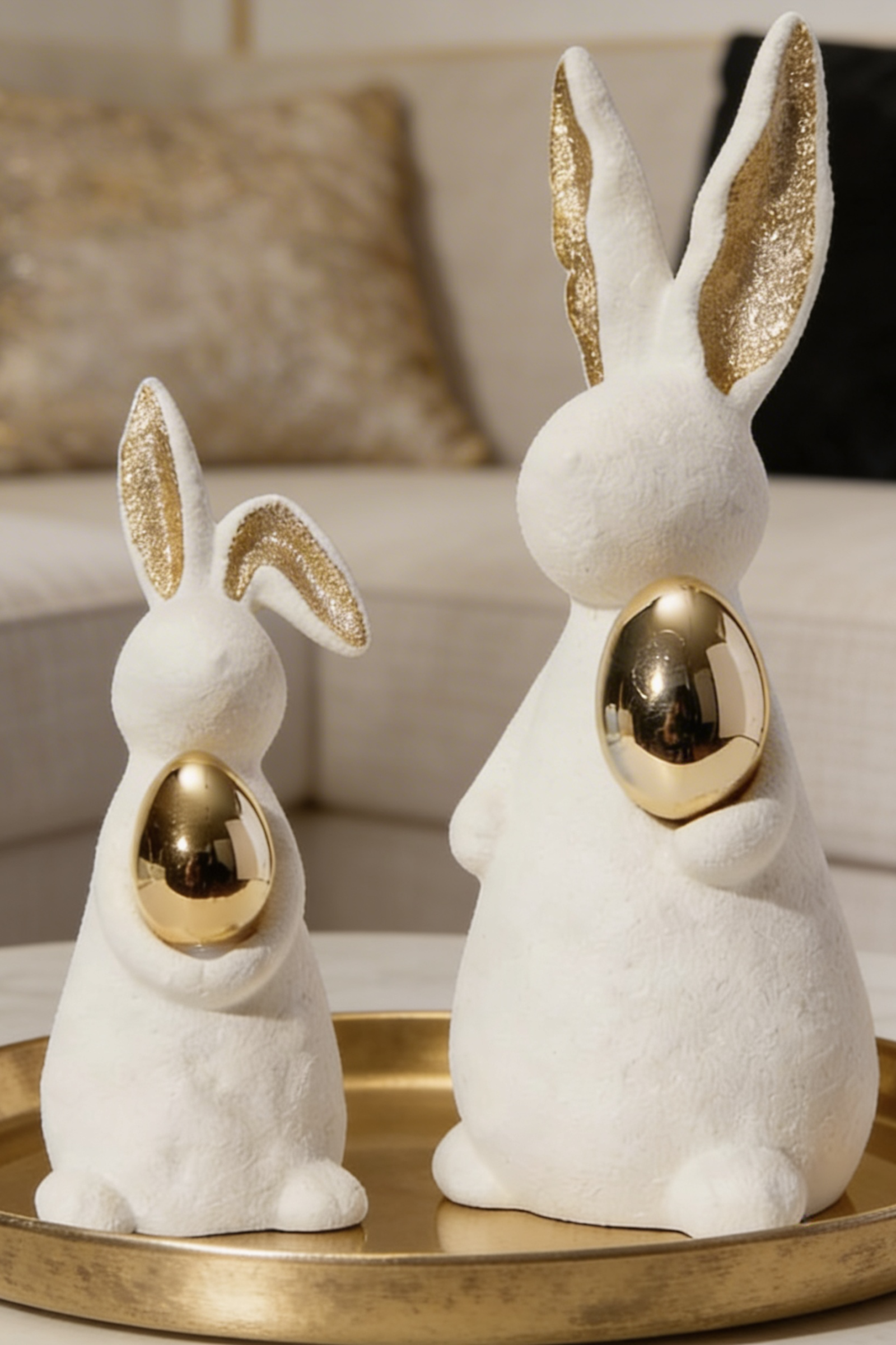 White velvet bunny figurines holding gold eggs with gold glitter ears displayed on a marble console with a gold leaf art canvas
